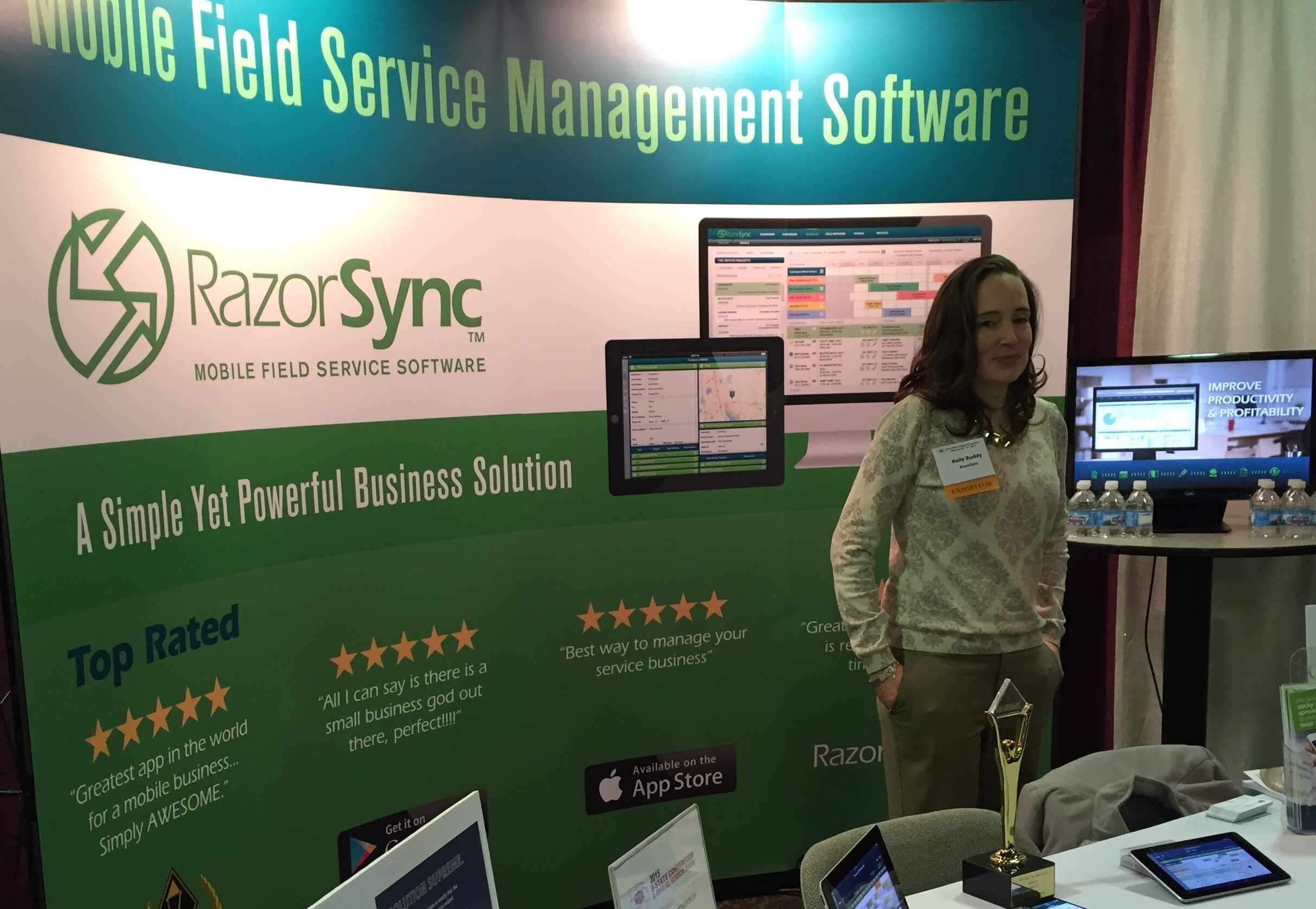 convention booth with banner reading mobile field service management software, razorsynd, a simple yet powerful business solution, and a young woman standing in front of a computer monitor