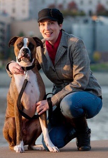 kelly ruddy kneeling by large boxer dog with city in background